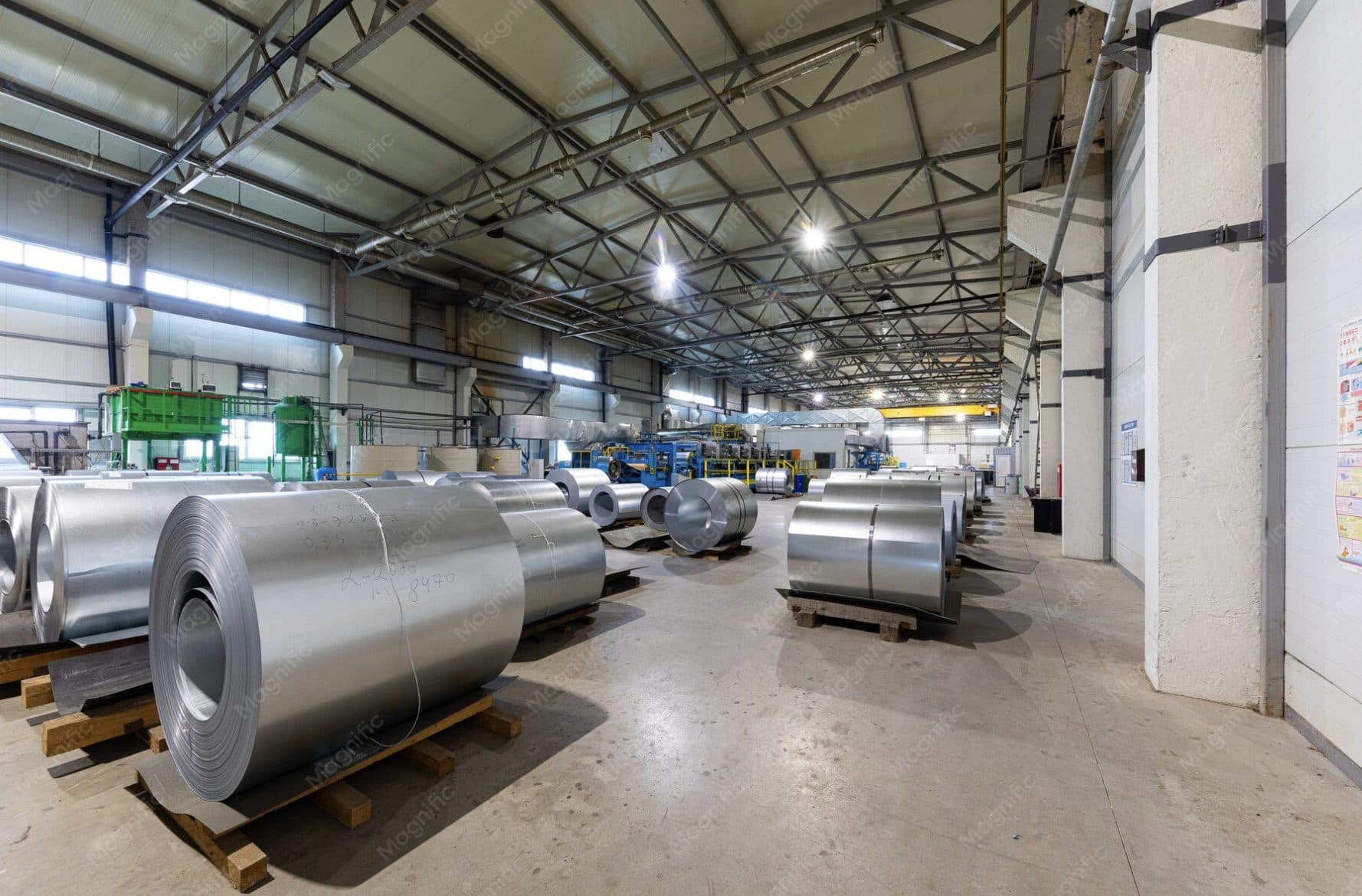 Steel coils stored on pallets inside an industrial production hall
